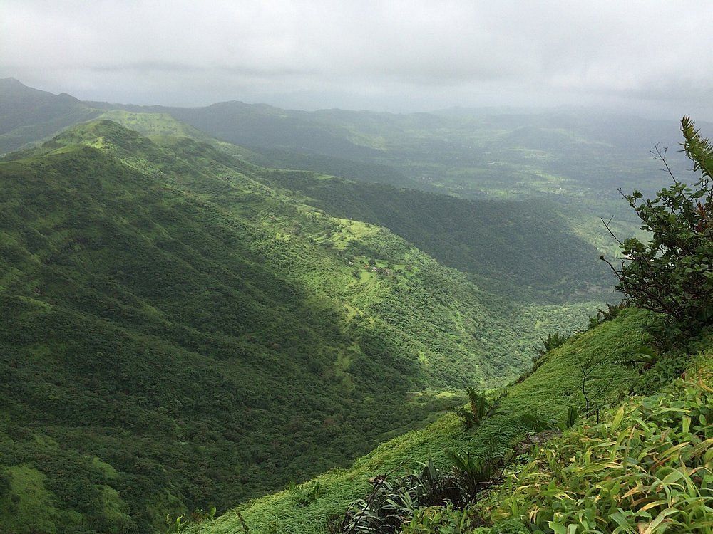 A panoramic view of the surrounding hills from the Sinhgad fort. The hills are covered in dense green vegetation, and the sky is cloudy.